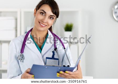Beautiful charming friendly smiling female medicine therapeutist doctor standing in office, holding document pad and looking in camera. Medical help, physician reception or insurance concept