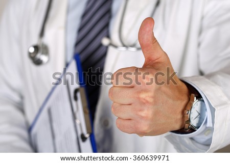 Male medicine doctor holding document pad in hand showing OK or approval sign with thumb up. High level and quality medical service, best treatment and patient care concept. Satisfied, happy intern