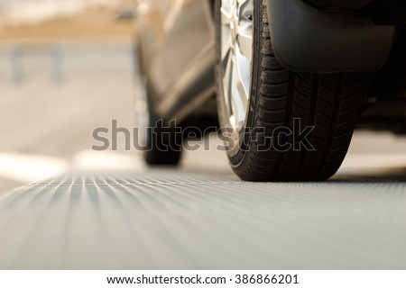 Dark automobile standing on steel floor view from below. Car parking problems, motor show or exhibition, winter season tires, customer purpose loan, vehicles official checkup or examination concept