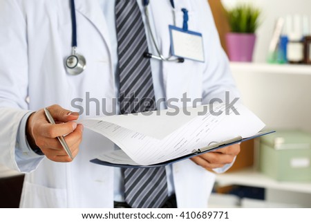 Male medicine doctor hand holding silver pen looking in clipboard closeup. Ward round, patient visit check, medical calculation and statistics concept. Physician ready to examine patient