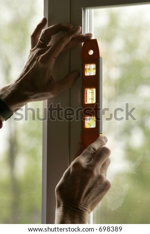 A pair of hands using a bubble level on a window.  Bubble is backlit