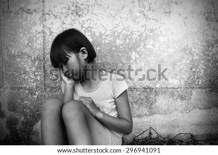 sad and depressed little girl sitting near the old wall on black and white