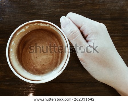 Hand holding a cup of Coffee Latte on dark wood table