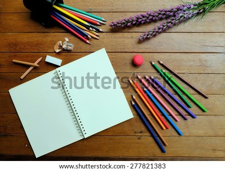 Blank white notebook with colored pencils on wood background decorated with purple flower