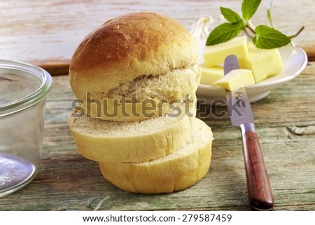 close up of small bred rolls / loaves of white bread on wooden surface with knife and butter