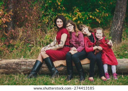mother and her three daughters, all wearing red, sitting on the log in the forest