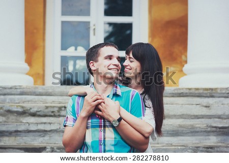 happy young couple walking near a beautiful house. Thin girl in a white dress and guy in shirt. Photo in warm colors.
