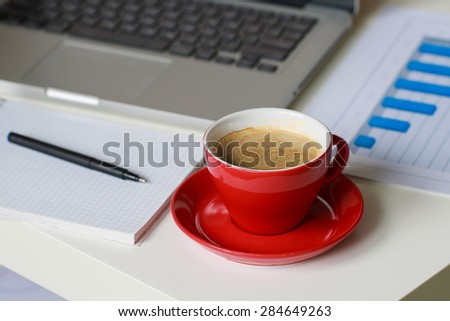 business diagrams, note book with black pen on it, red cup of coffee and silver laptop on the table
