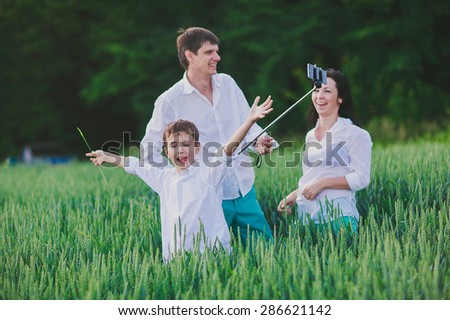 a happy family is taking photos of themselves with the help of monopod in the green field