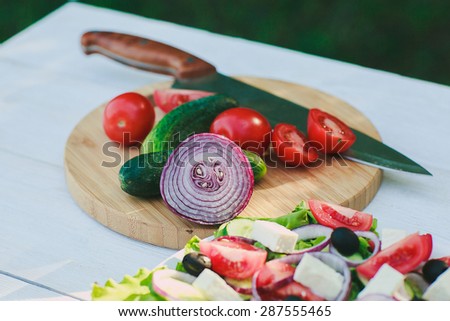 Fresh tomatoes and onions cut into pieces, cucumber and knife on a white wooden table