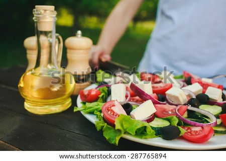 a chef finished cooking, greek salad, olive oil and some spices on a dark wooden table