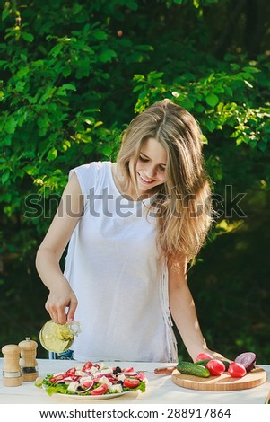 a girl is pouring olive oil into Greek salad, cooking outdoors