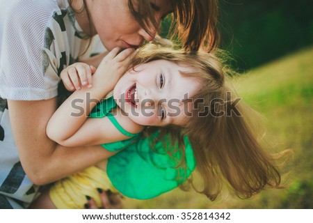 mother is holding her happy daughter and kissing her cheek
