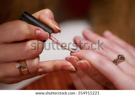 a manicure master is covering nails of her client with a nail polish