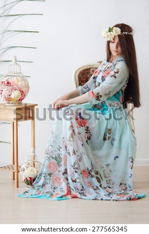 Modest girl is sitting on the chair in floral dress and crown
