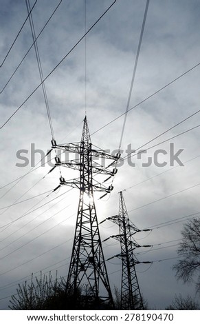 Sun shine through clouds over pylons of high voltage power line