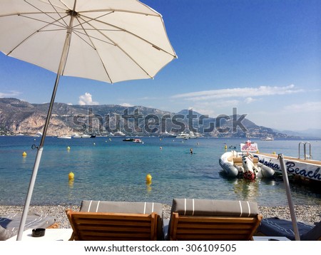 beach club in the south of france/ Paloma beach/ St jean cap ferrat, France - September 5, 2014: View of the Mediterranean with Two empty lounge chairs on paloma beach with parasol and rubber boat