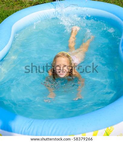 A smiling girl bathes in pool and sprays water