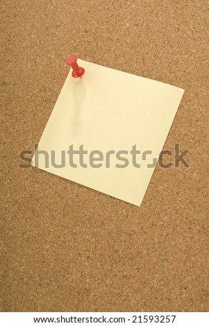 Red push pin holding a square note to a cork board.