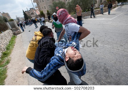 BETHLEHEM, OCCUPIED PALESTINIAN TERRITORIES - MARCH 30: A Palestinian overcome by tear gas is carried to safety during Land Day protests at the Bethlehem checkpoint on March 30, 2012.
