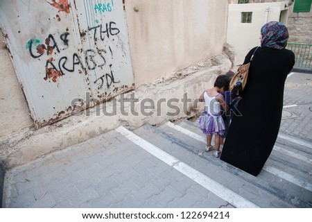 HEBRON, PALESTINIAN TERRITORY - OCTOBER 22: A Palestinian woman and children pass the slogan \