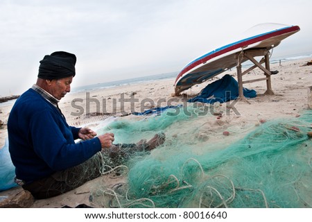 GAZA CITY, OCCUPIED PALESTINIAN TERRITORIES - FEBRUARY 3: A Palestinian fisherman mends his nets on Gaza City\'s beach on Feb. 3, 2011. Israeli restrictions have severely impacted Gaza\'s fishing trade.
