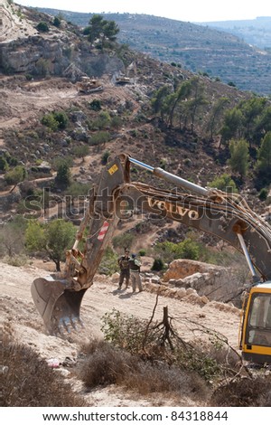 AL-WALAJA, OCCUPIED PALESTINIAN TERRITORIES - SEPTEMBER 5: An Israeli soldier guards equipment near a pile of olive trees cut down to make way for the Israeli separation barrier on Sept 5, 2001.