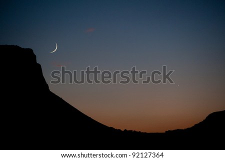 In the glow of sunset, a slim crescent moon and evening star hang in the sky over the Arbel Cliffs near the Sea of Galilee in northern Israel.