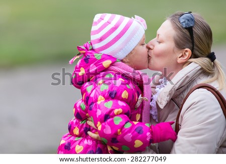 Mother and daughter are kissing each other in the park. (Late fall)