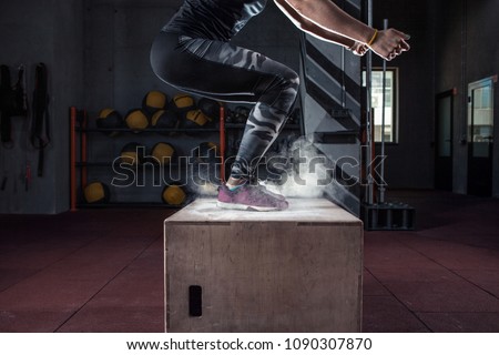 Young woman jumping box and talc powder departs from under feet. Fitness woman doing box jump workout at cross fit gym.