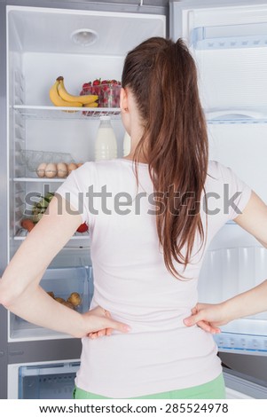 Young woman craving food choosing near refrigerator