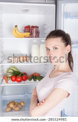 portrait of  serious female standing near open refrigerator, healthy lifestyle concept