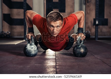 Handsome muscular man doing push ups on kettle ball in  gym