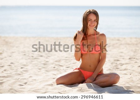 Beautiful girl in a swimwear on a sandy beach with flash tattoo on her in front of the sea with free space