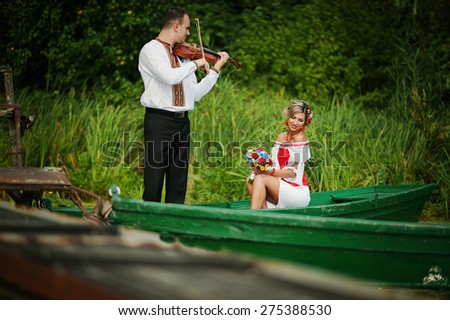 Wedding beautiful couple in traditional dress on the dock . Groom playing the violin