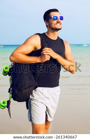 Young  stylish men posing on  the  beachfront  with skateboard.Wear cool and  stylish clothes.Happy  with the  life.Wear  sunglasses.