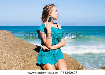 Sexy woman with perfect skin  posing on the  beachfront near rocks and wear stylish summer clothes.Summer swimwear,cool accessories,blonde hair,blue dress,summer mood,hipster girl in summer dress.