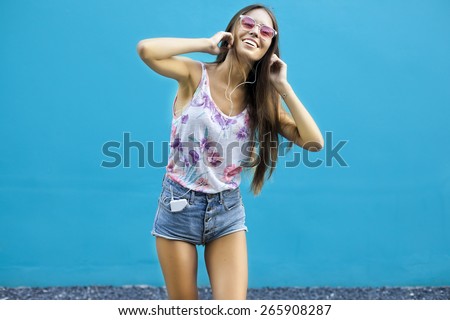 young beautiful happy stylish hipster girl,listen music,summer outfit, smiling, fashion, teen,cool accessories, purse,mans sunglasses,amazed, vintage style, wall background, hair, wind