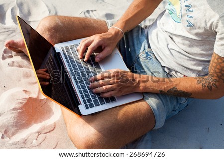 Young  man working with computer on the beach. Handsome man working with laptop laying on the couch at the beach. Empty display for your screen shot.