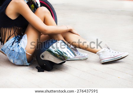 Young sexy blonde woman sitting on the street,with helmet opposite motorbike.Lifestyle portrait bright toned colors,cool rock n roll girl, wear summer outfit, bright summer clothes,denim shorts