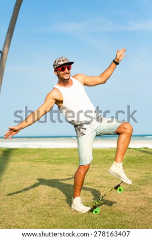 Young handsome hipster man relaxed at sunny day on the park, and stylish.Summer men sunglasses,hipster boy with long board,denim shorts,cool hipster cap,b-boy,tropical sexy man
