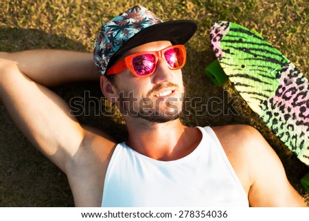 Young handsome hipster man relaxed and  lay at sunny day on the park on tropical island in cool summer sunglasses,reflecting palm trees in sunglasses.Stylish young beard man,hipster outfit.