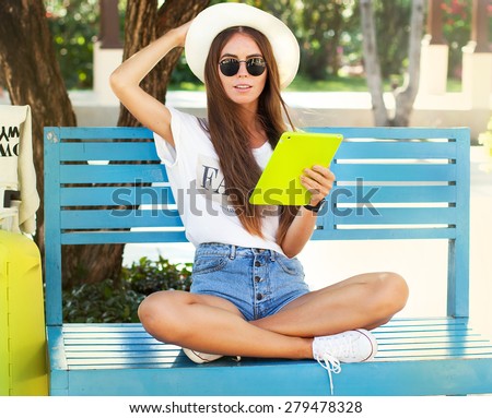 closeup of happy woman in glasses using tablet pc in the park Young woman wearing stylish hipster outfit,straw hat,travel concept photo,soft image,airport departure,arrived,car trip,California.street