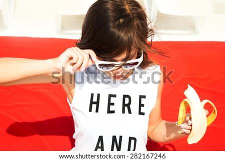 Young stylish sexy pretty hipster girl having fun, on the beach,and eating fruits. Funny image of  woman eating big banana and having fun.Sunshine sunglasses,Hare and now