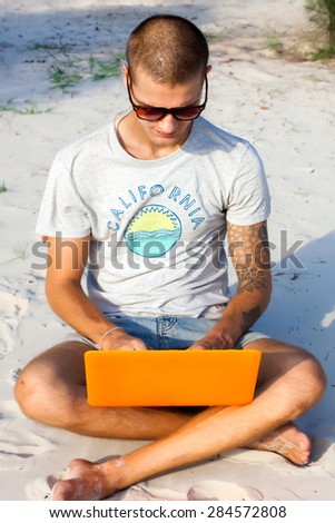 Handsome young man posing on the  beach and working on laptop on internet. Freelance work,travel concept,hike man,social network,man with computer on the beach,working on the beach of tropical island