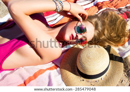 Fashion outdoor travel photo of sexy beautiful woman with blond hair in elegant summer bikini and accessories,summer mirrored sunglasses and travel hat,relaxing on tropical summer beach,summer colors