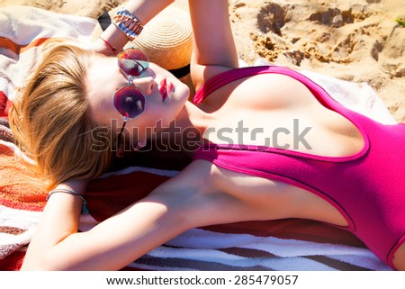 Young sexy woman laying and relaxed at the beach at summer holidays,at hot day,wearing sexy trendy bikini and reflecting woman's fashionable sunglasses,enjoy summer.Bright warm colors,summer accessory