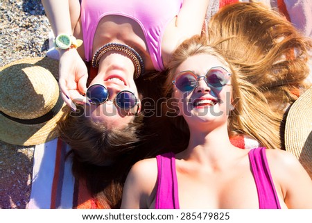 Attractive best friends having fun on the beach,Girls Laughing and having fun on beach.summer holidays and vacation-girls sunbathing on the beach.Summer things and accessorize,trendy bikini,sunglasses