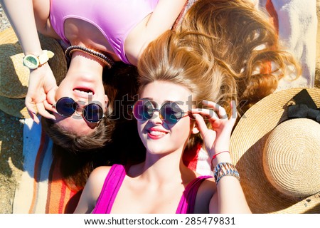 Attractive best friends having fun on the beach in summer.Laughing and having fun.Two young teenage girls looking on camera and sending you air kiss,wear bikini sunglasses and fashion bright jewelry