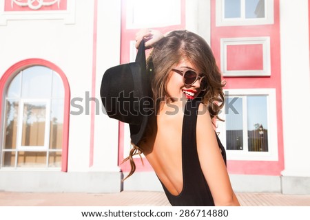 Close-up Fashion woman portrait of young pretty trendy girl posing at the city in Europe,summer street fashion,holding retro fedora hat popular until the 60s.laughing and smiling portrait.trendy chic